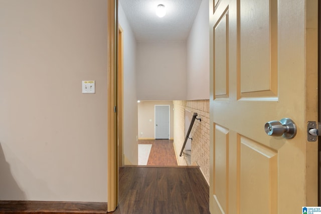 corridor with a textured ceiling, baseboards, an upstairs landing, and wood finished floors