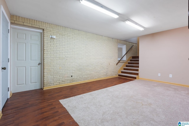 finished basement featuring stairway, baseboards, brick wall, and wood finished floors