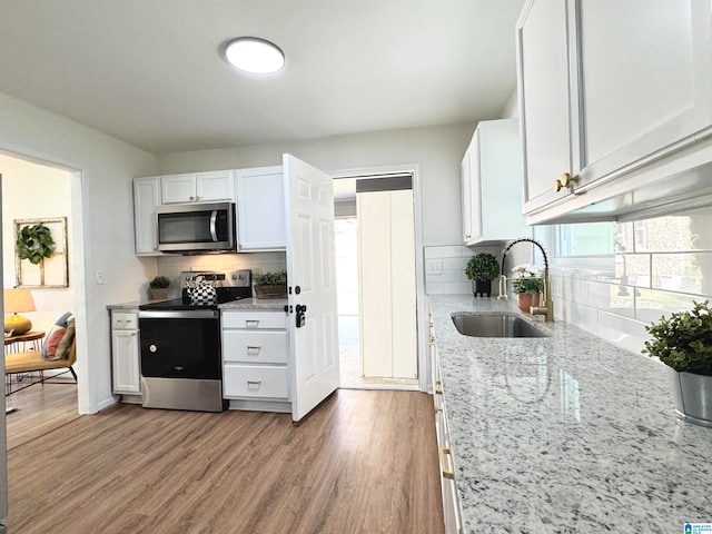 kitchen featuring light stone counters, sink, light hardwood / wood-style flooring, white cabinetry, and stainless steel appliances