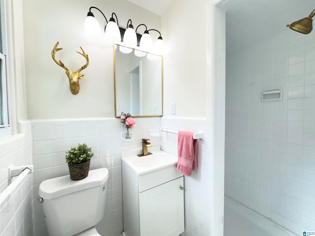 bathroom with tile walls, tiled shower, vanity, and toilet