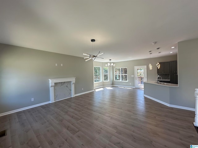 unfurnished living room featuring sink, dark wood-type flooring, and a notable chandelier