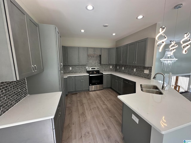 kitchen with hanging light fixtures, sink, stainless steel stove, gray cabinets, and light wood-type flooring