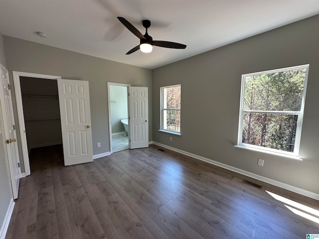 unfurnished bedroom with ceiling fan, connected bathroom, a walk in closet, hardwood / wood-style flooring, and a closet