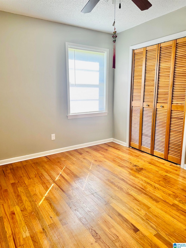 unfurnished bedroom with a closet, light wood-type flooring, a textured ceiling, and ceiling fan