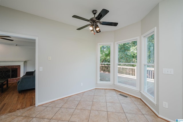 unfurnished room with ceiling fan, light tile patterned flooring, and a fireplace