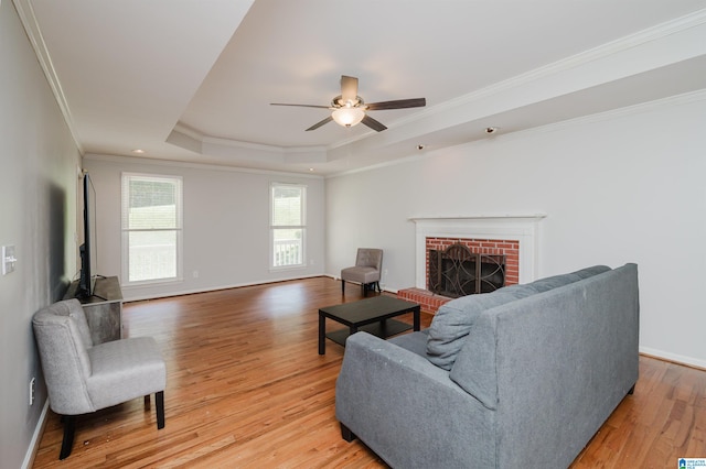 living room with wood-type flooring, a tray ceiling, a fireplace, crown molding, and ceiling fan