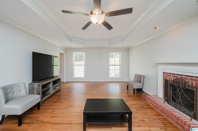 living room featuring a raised ceiling, a fireplace, ceiling fan, light hardwood / wood-style flooring, and ornamental molding