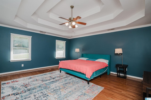 bedroom featuring ceiling fan, ornamental molding, a tray ceiling, and hardwood / wood-style floors