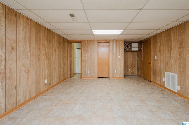 unfurnished room featuring wood walls and a paneled ceiling