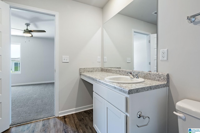half bathroom with baseboards, ceiling fan, wood finished floors, toilet, and vanity
