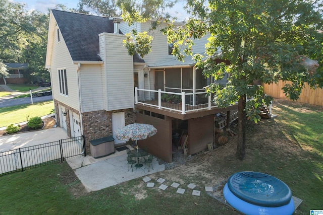 back of house featuring a lawn, a garage, a sunroom, and a patio area