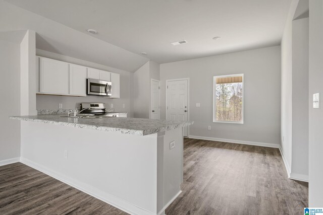 kitchen with kitchen peninsula, dark hardwood / wood-style floors, stainless steel appliances, and white cabinets