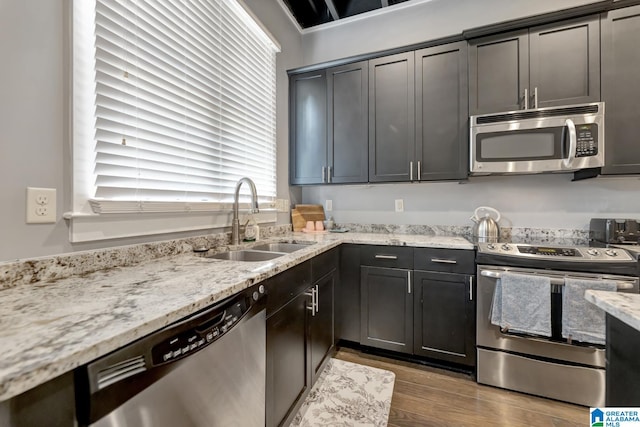 kitchen with wood-type flooring, stainless steel appliances, light stone counters, and sink