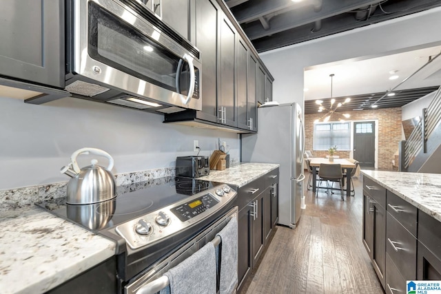 kitchen featuring pendant lighting, light stone counters, stainless steel appliances, dark hardwood / wood-style flooring, and brick wall