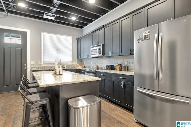 kitchen featuring hardwood / wood-style flooring, stainless steel appliances, a center island, light stone countertops, and a kitchen bar