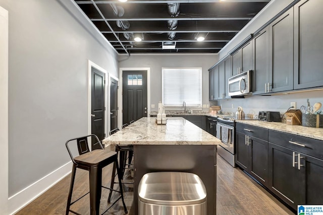 kitchen with a kitchen breakfast bar, light stone counters, a kitchen island, dark hardwood / wood-style flooring, and stainless steel appliances