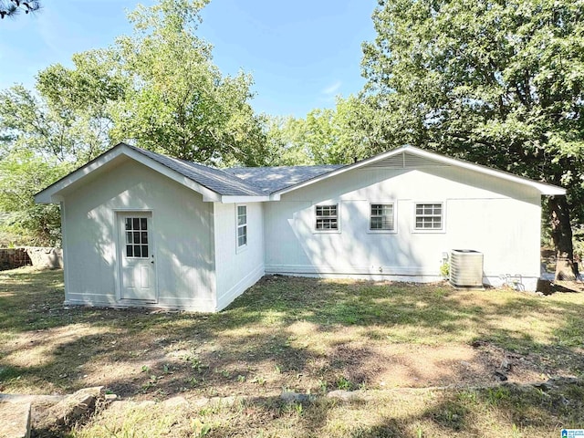 rear view of house featuring central AC unit and a lawn