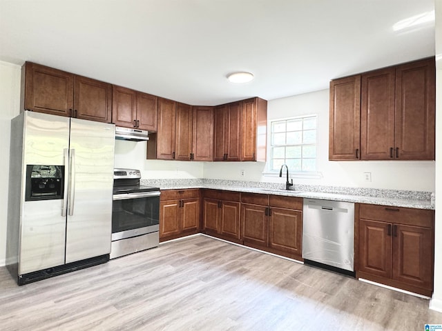 kitchen featuring appliances with stainless steel finishes, light stone countertops, sink, and light hardwood / wood-style flooring