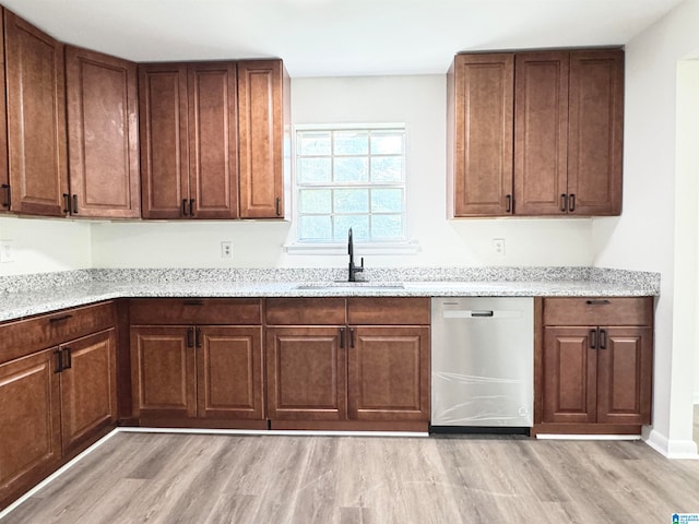 kitchen with light stone counters, light wood-type flooring, sink, and stainless steel dishwasher