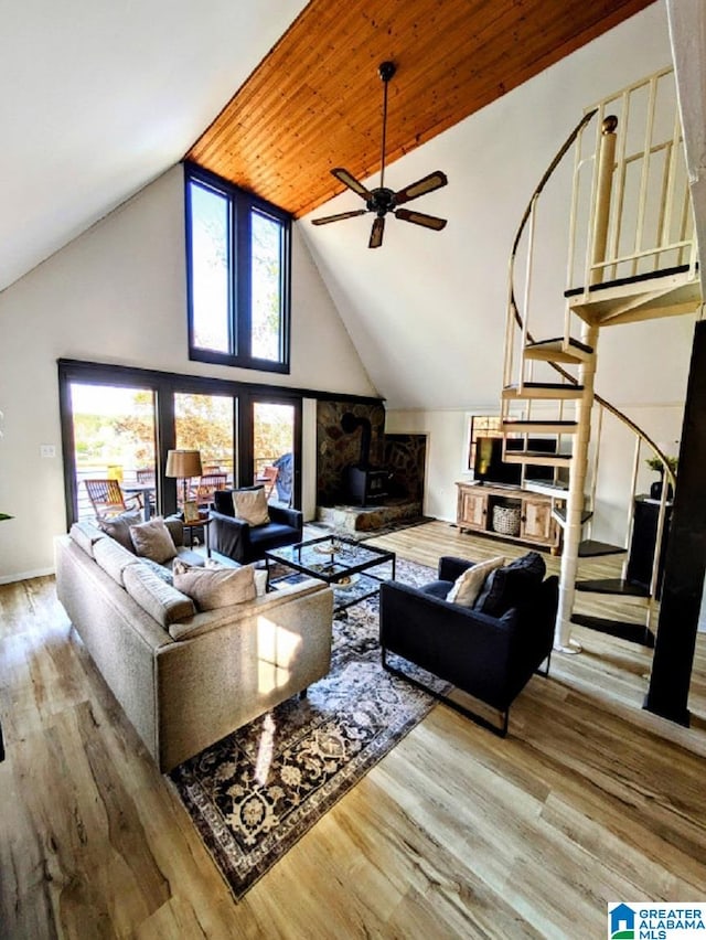 living room featuring wood ceiling, light hardwood / wood-style floors, a wood stove, high vaulted ceiling, and ceiling fan