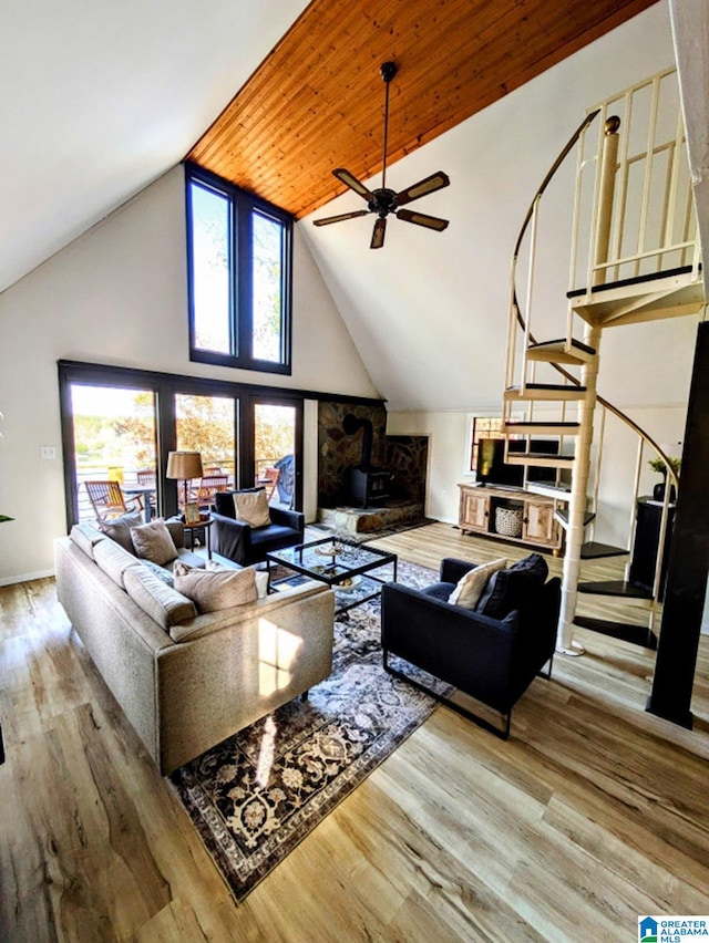 living room with ceiling fan, a stone fireplace, light hardwood / wood-style flooring, and high vaulted ceiling