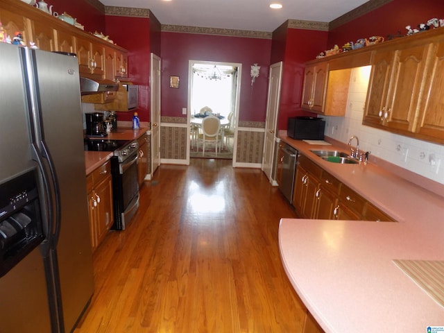 kitchen with appliances with stainless steel finishes, crown molding, sink, and light hardwood / wood-style flooring