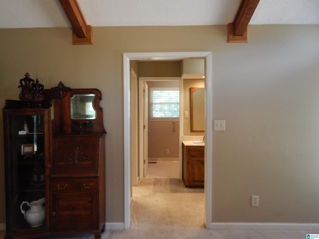 hallway featuring beam ceiling, a textured ceiling, and light colored carpet