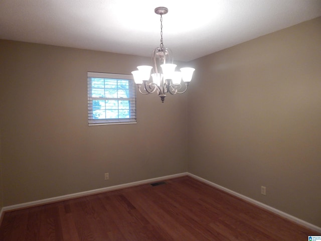 spare room featuring an inviting chandelier and dark wood-type flooring