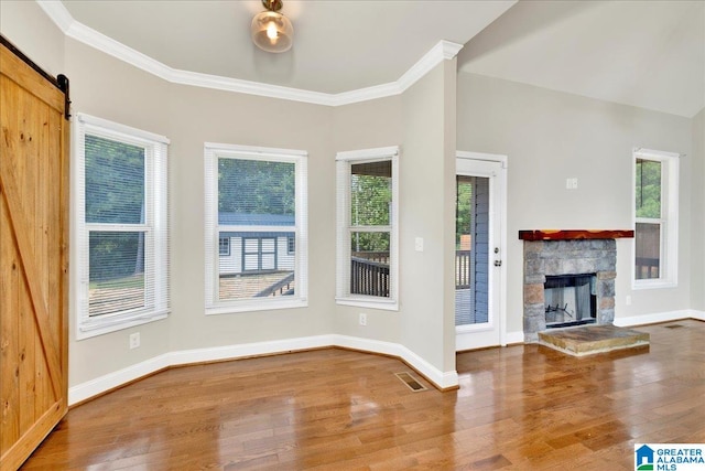 unfurnished living room featuring a stone fireplace, a wealth of natural light, hardwood / wood-style flooring, and a barn door