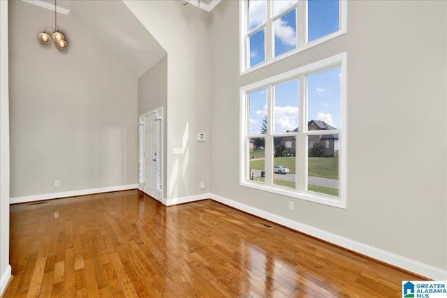 unfurnished living room with an inviting chandelier, a high ceiling, and hardwood / wood-style floors