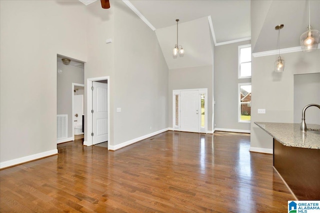 unfurnished living room featuring ceiling fan, crown molding, dark hardwood / wood-style floors, and high vaulted ceiling