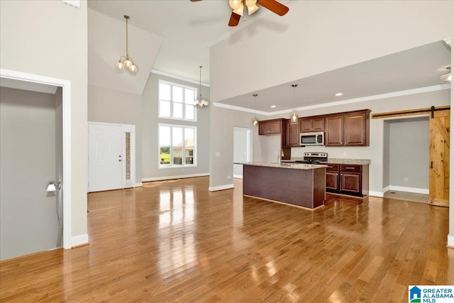 kitchen featuring wood-type flooring, appliances with stainless steel finishes, a high ceiling, ceiling fan with notable chandelier, and a barn door