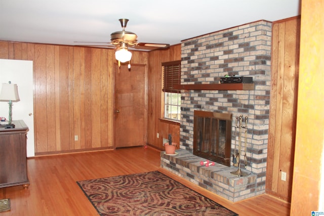 living room featuring light hardwood / wood-style flooring, wood walls, ceiling fan, and a fireplace