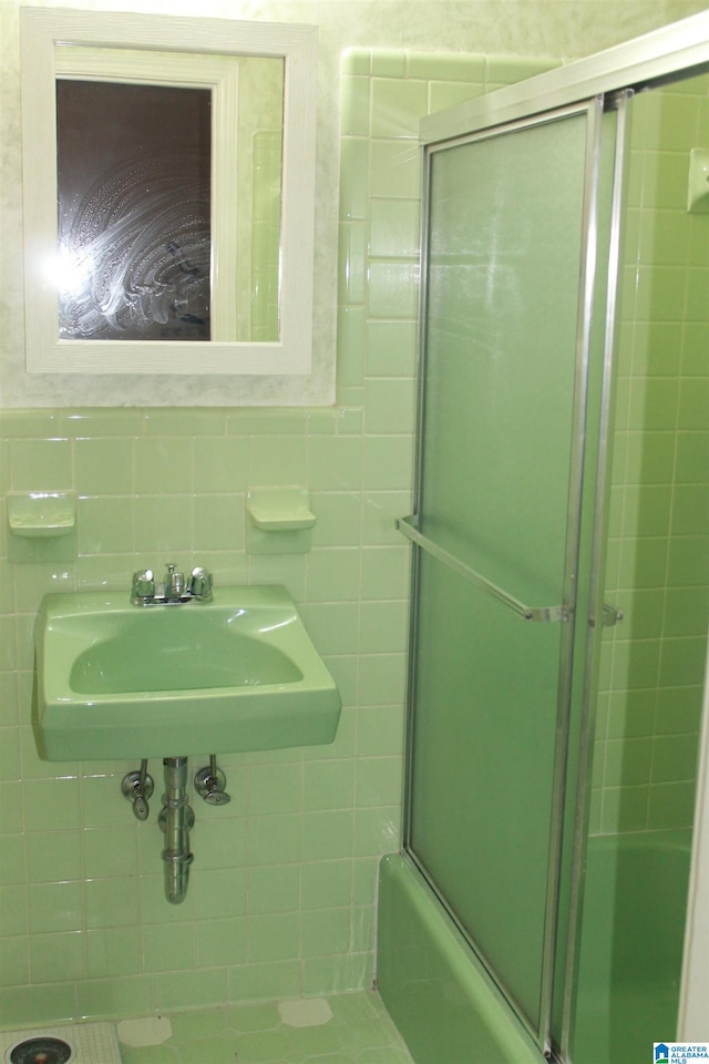 bathroom featuring tile walls, sink, and combined bath / shower with glass door