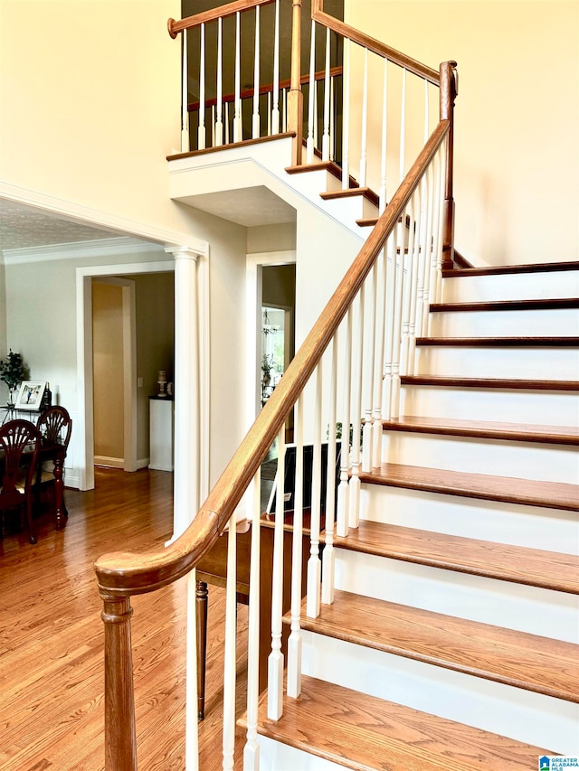 staircase featuring ornate columns, hardwood / wood-style floors, and crown molding