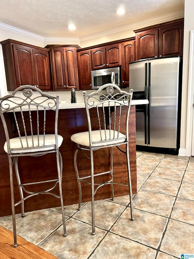 kitchen featuring a textured ceiling, a kitchen breakfast bar, appliances with stainless steel finishes, light tile patterned floors, and crown molding