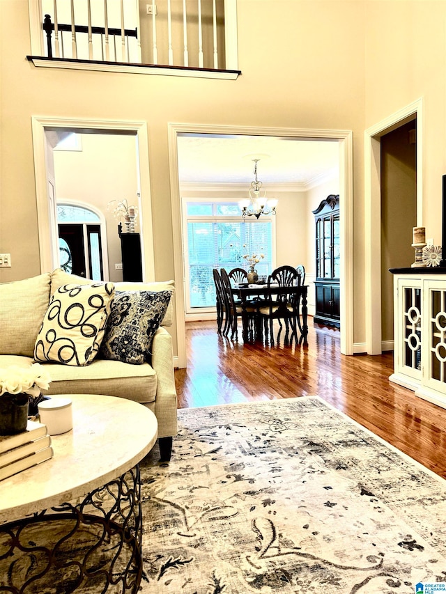 living room featuring a notable chandelier, hardwood / wood-style flooring, crown molding, and a high ceiling