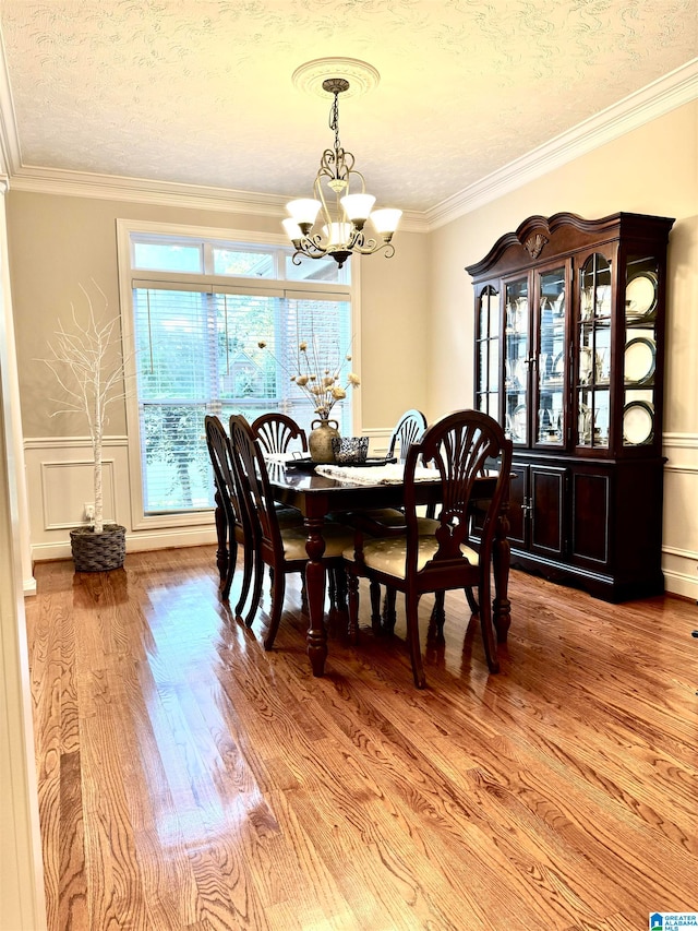 dining space featuring a textured ceiling, light hardwood / wood-style floors, ornamental molding, and a notable chandelier