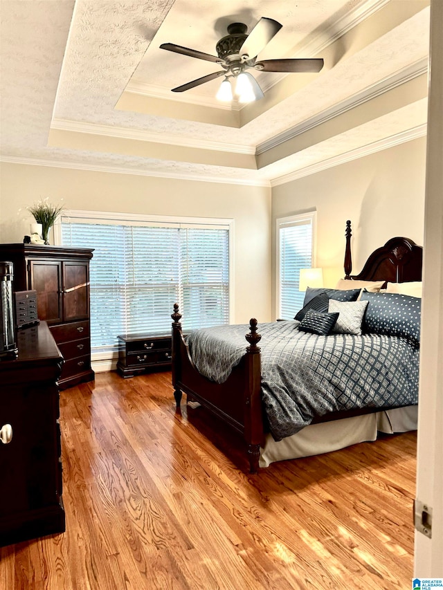 bedroom featuring ceiling fan, a tray ceiling, light wood-type flooring, and ornamental molding