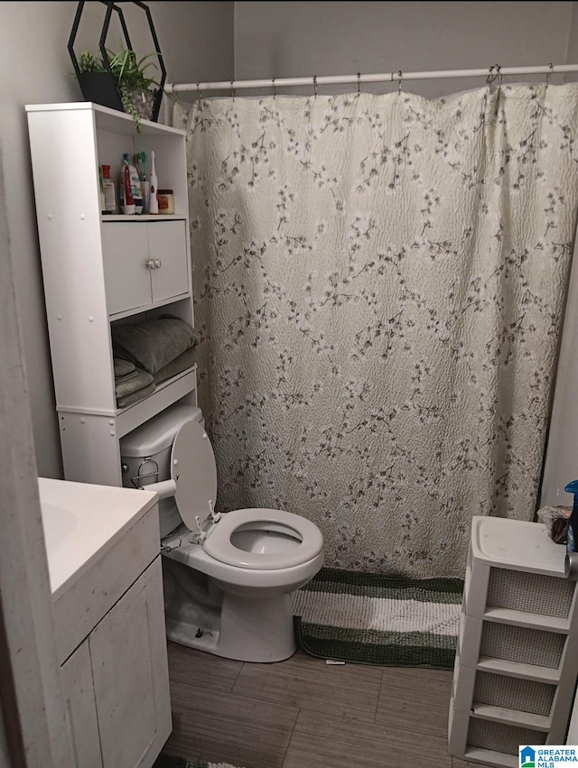 bathroom with wood-type flooring, walk in shower, vanity, and toilet