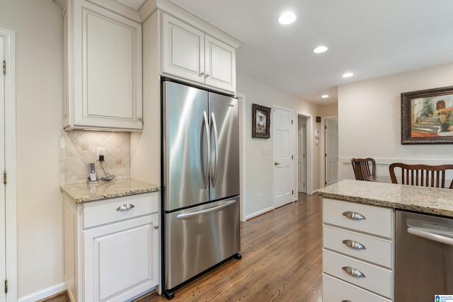 kitchen featuring light stone counters, tasteful backsplash, white cabinetry, hardwood / wood-style flooring, and appliances with stainless steel finishes