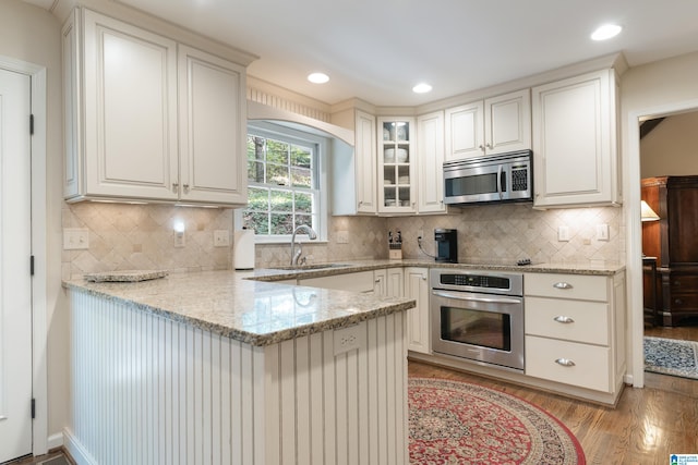 kitchen featuring appliances with stainless steel finishes, light stone counters, white cabinets, light hardwood / wood-style flooring, and sink