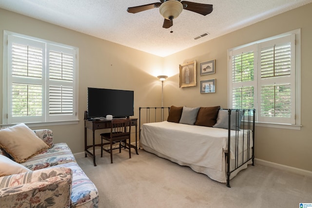 carpeted bedroom featuring ceiling fan, a textured ceiling, and multiple windows