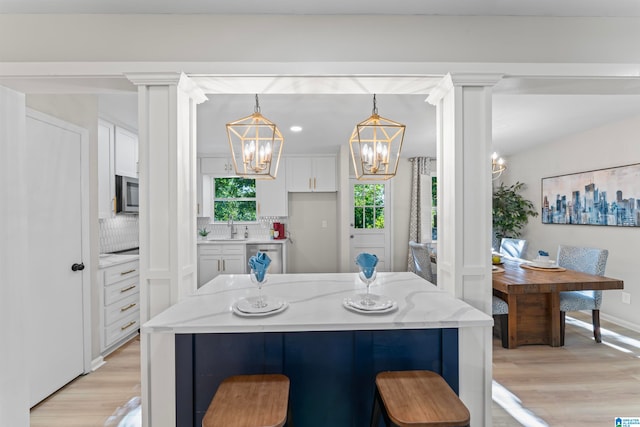 kitchen with decorative backsplash, a kitchen breakfast bar, sink, pendant lighting, and white cabinetry