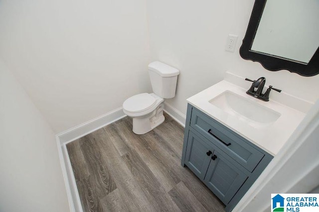 half bathroom featuring baseboards, wood finished floors, toilet, and vanity