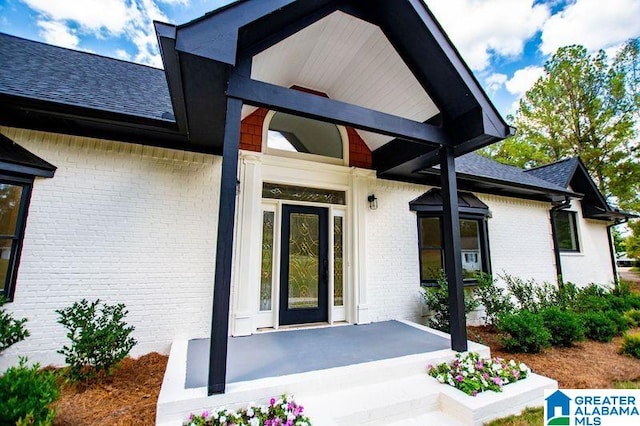 view of exterior entry featuring brick siding and a shingled roof