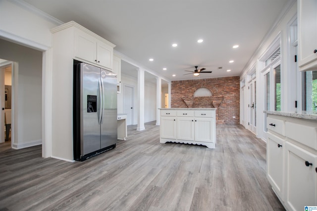 kitchen featuring white cabinetry, ceiling fan, stainless steel fridge, and brick wall