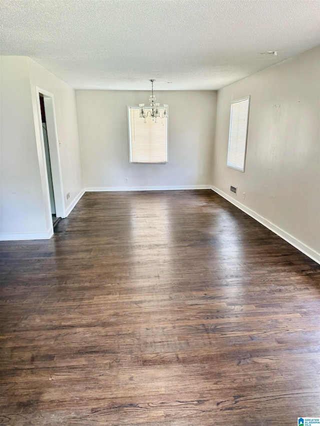 spare room featuring dark wood-type flooring, a chandelier, and a textured ceiling