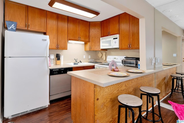 kitchen with white appliances, dark hardwood / wood-style floors, sink, and a kitchen bar