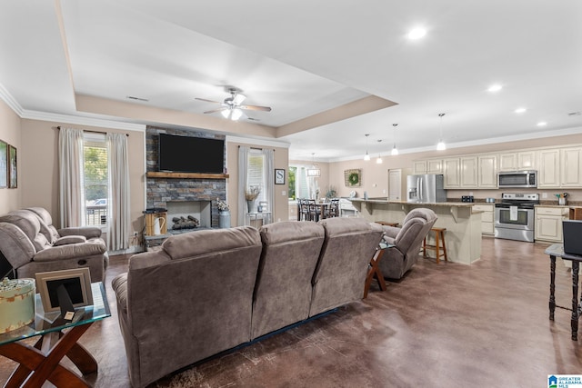 living room with ornamental molding, ceiling fan, a raised ceiling, and a fireplace